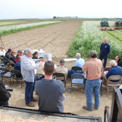 Cooperative Extension academics sharing information with farmers at study site, which is a farm with two tractors in the background.
