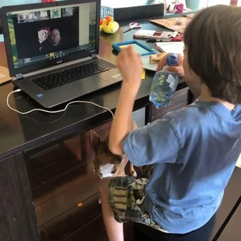 Youth drinks a bottle of water while sitting in front of a laptop. On the laptop is the Zoom application showing the video of a 4-H Advisor.