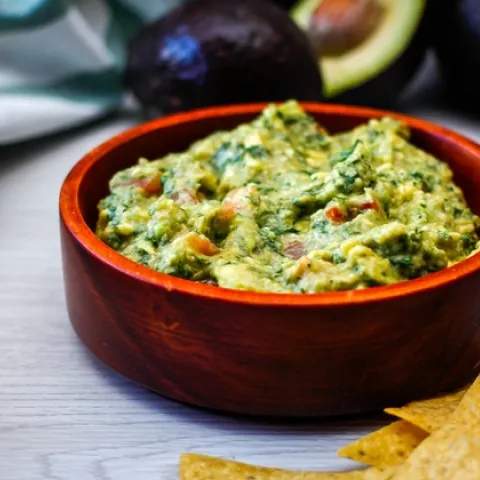 Bowl of guacamole with tortilla chips on the side.