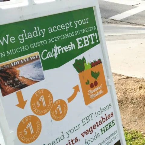 A tent sign reads: "We gladly accept your CalFresh EBT" and "En mucho gusto aceptamos su tarjeta." "Spend your EBT toekns on fruits, vegetables and other healthy foods HERE.