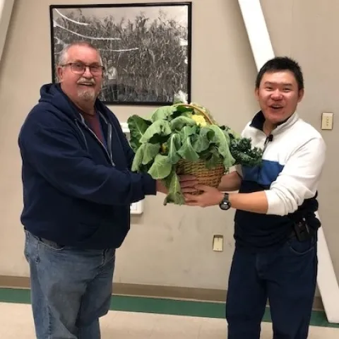 Master Gardener hands instructor gift basket with kale, cauliflower, and other vegetables.