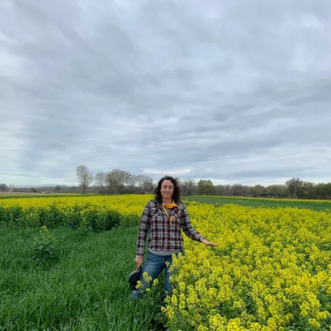 Sarah Light stands next to waist-high yellow blooms in a field of white mustard.