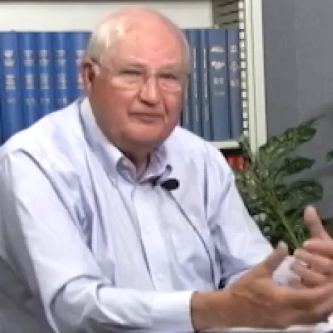 Jim Clawson sitting in front of a bookcase and a potted plant.