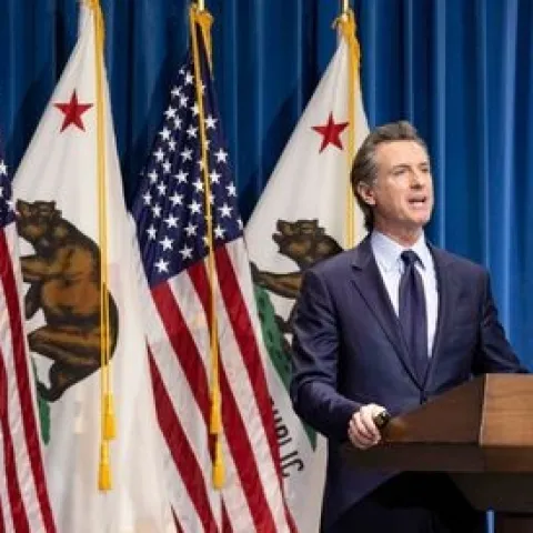 The governor stands at a lectern in front of four flags -- 2 US flags and 2 California flags alternating.