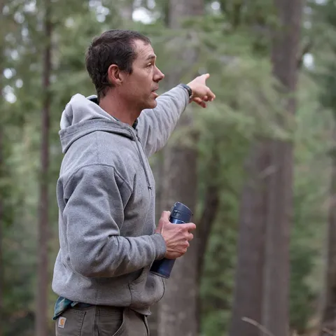 Rob York, holding a water bottle in his right hand, points into the forest with his left hand.