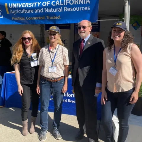 The four are standing in front of the Master Gardener booth under a banner that reads: University of California Agriculture and Natural Resources. Practical. Connected. Trusted.