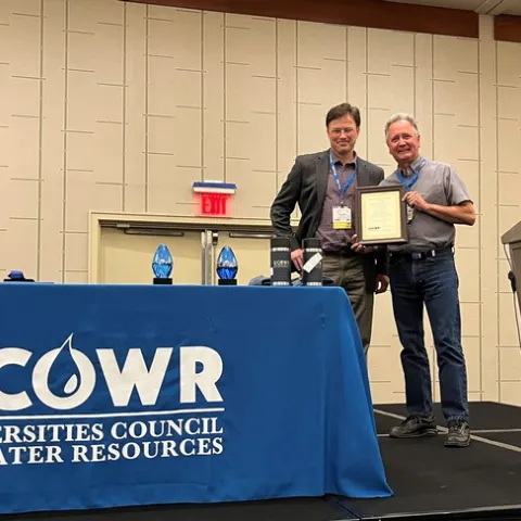 Two men standing on stage with plaque.