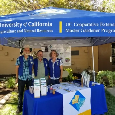 Three Master Gardeners smiling and standing underneath a blue tent.