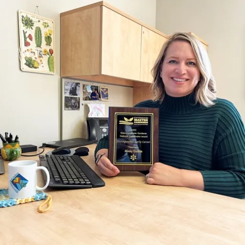 Missy at in her office holding up her award plaque.