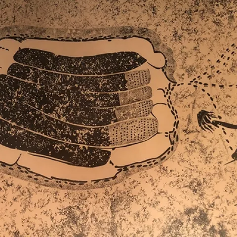 This framed photo of an image, once belonging to the late Extension apiculturist Eric Mussen, shows an ancient rock painting from Zimbabwe. A beekeeper is using a smoker.