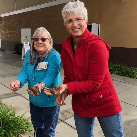 Two women holding soil samples and smiling.