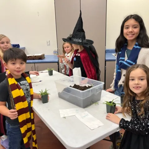 Smiling children gathered around a table using pots, plants, and soils for the activity.