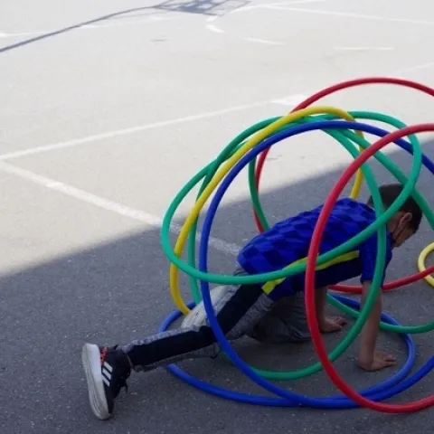 A child surrounded by red, green, blue and yellow hoops on a playground stretches his leg.