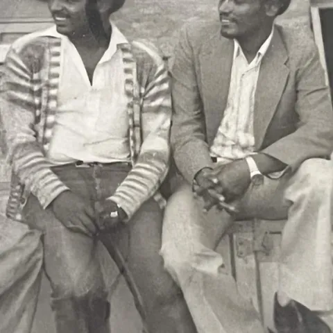 Two men sitting against a wall, looking off camera.