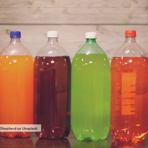 Two-liter plastic bottles of assorted colors of soda in a line.