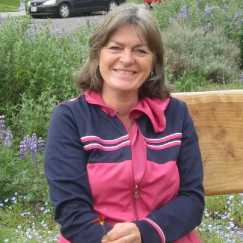 Author sitting on bench with a background of wildflowers.