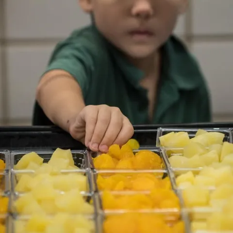 A young boy reaches for fruit in the cafeteria lunch line.
