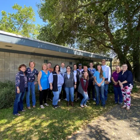 A group of people pose standing under a leafy tree.