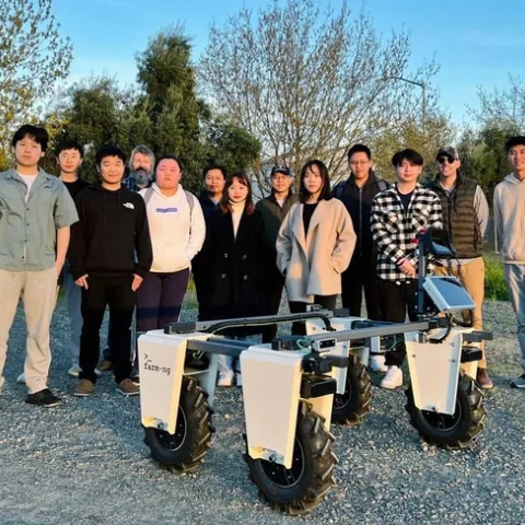 13 people stand around the Amiggie robot