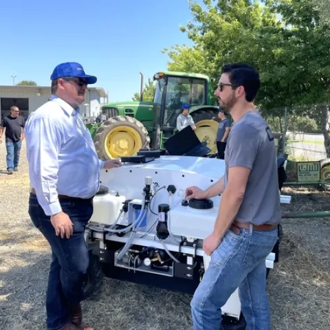 Gabe Youtsey converses while standing next to a robot with agricultural applications