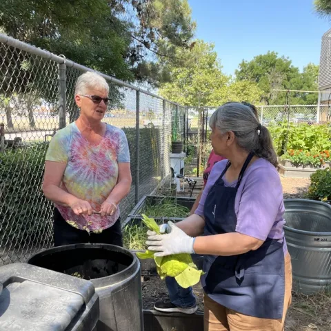 Two people standing next to a compost bin.