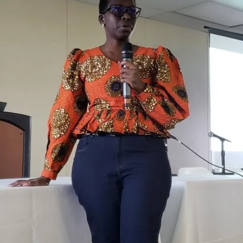 Woman wearing an orange print blouse speaks into a handheld mic.