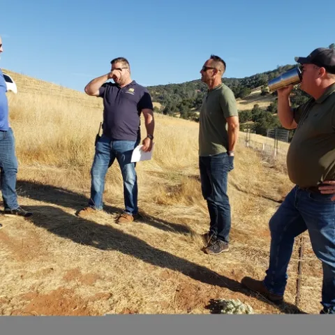 Four men standing on a hillside surrounded by dry grass.