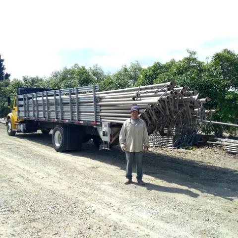 Santos stands beside a long flatbed truck loaded with irrigation pipes.