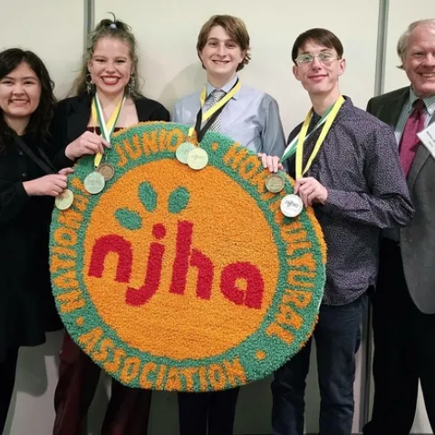 4 youth holding their medals and a round rug with the logo of NJHA, standing next to an adult in a suit and name badge