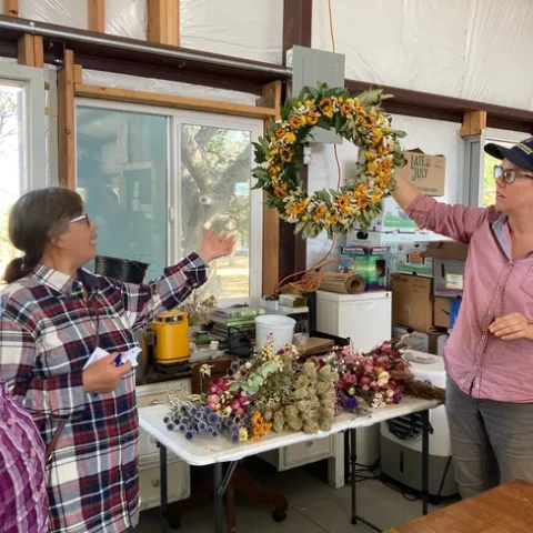 Lauren holds up a wreath made of greens and yellow flowers.