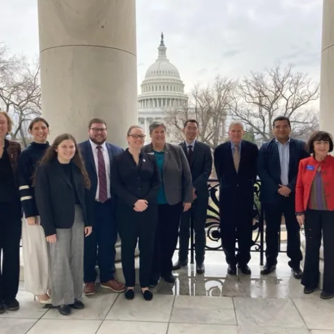 Group of people stand with U.S. capitol in the background.