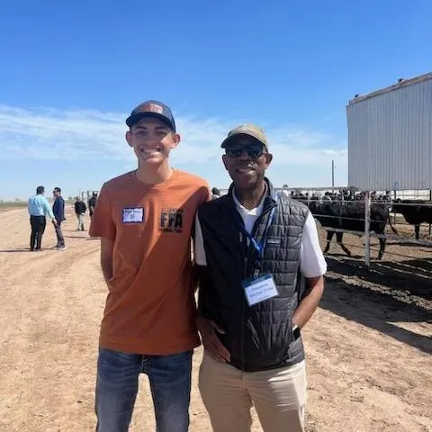 Young man stands next to President Drake with cows in the background.