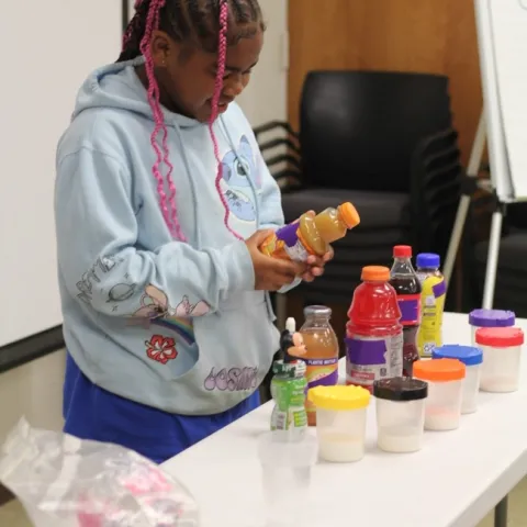 A young girl reads the back of an orange juice bottle.