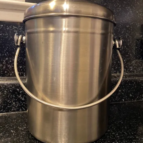 A silver, stainless steel pail with a handle and lid sitting on a kitchen counter.