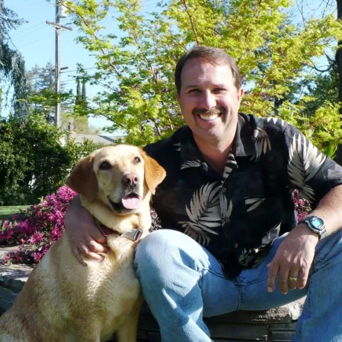 Roger sits beside his dog, a golden lab.