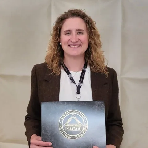 Laura Snell holds a plaque with the logo of the National Association of County Agricultural Agents.