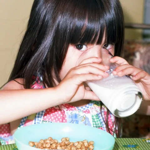 Toddler-age girl drinking milk from a glass.