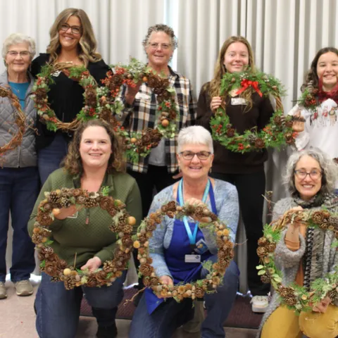 Smiling women in a group holding wreaths they made.