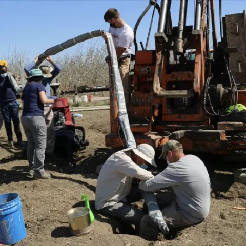 Seven people in an unplanted field collect data.
