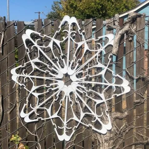 white plastic hangers connected into circular snowflake like design and mounted on a wood and chain link metal fence