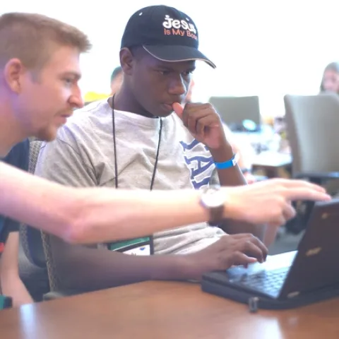 Adult pointing at laptop screen in front of youth