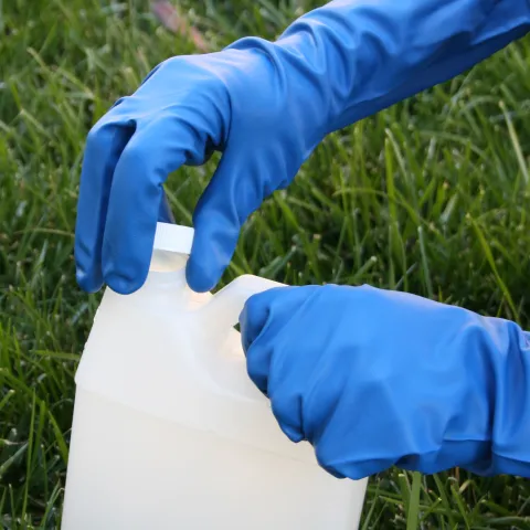 A person wearing blue gloves on their hands is unscrewing the cap to a white container
