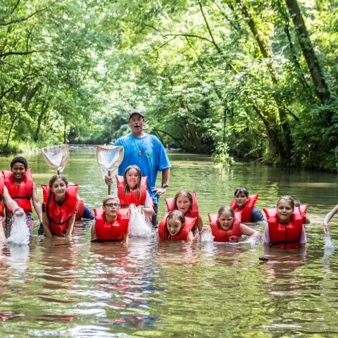 Adult with youth in lifejackets in river, holding nets