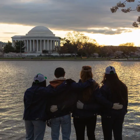 Back of 4 teens looking over water at the Jefferson Memorial at sunset