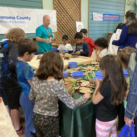 Kids gather around a table covered in cardboard parts and connectors.