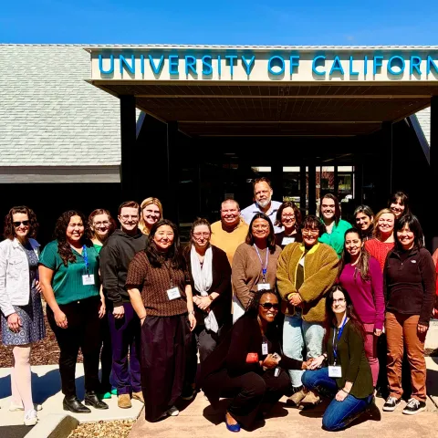 a group of 25 people in front of a Univ of California sign