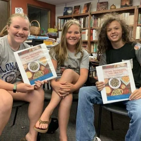 Young people at Foothill Indian Education Alliance facility pose with a cookbook of Native recipes
