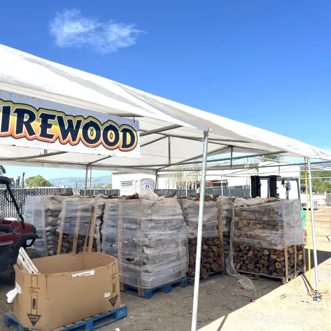 Stacks of firewood for sale below a canopy with a sign that says "firewood."