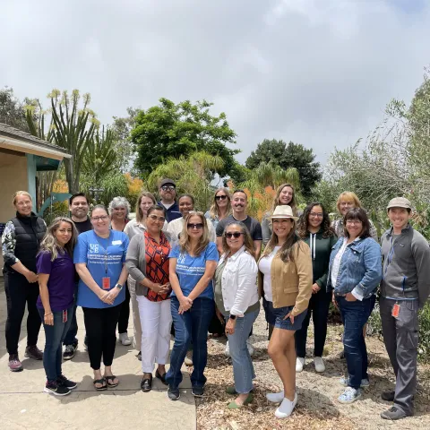Nineteen people stand outdoors posing for a photo