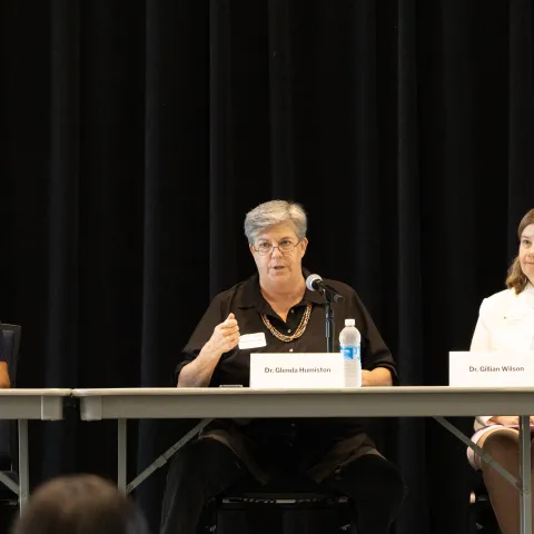 Srabani Glenda and Gillian sit at a long table facing the audience. Glenda is speaking into a mic